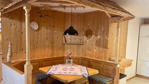 A wooden dining area with a table and benches, a clock, and a shelf with glassware. - Charmante Ferienwohnung Handweberei mit Garten und Liegewiese, Wlan, 130 qm, Parkplatz (Saaldorf-Surheim)