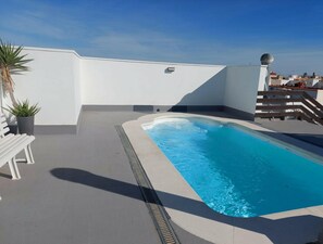 Une piscine sur le toit, avec un mur blanc et un escalier en bois.