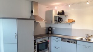 A modern kitchen with white cabinetry, a built-in oven, a coffee maker, and a dishwasher. - Apartment "Bieniussa 3" with Private Garden & Wi-Fi (Gemünden am Main)