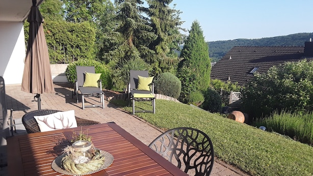 An outdoor patio with a wooden table, two chairs, and an umbrella. - Apartment "Bieniussa 3" with Private Garden & Wi-Fi (Gemünden am Main)