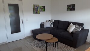 A living room with a dark sofa, a small round table, a patterned rug, and two wall-mounted pictures. - Apartment "Bieniussa 3" with Private Garden & Wi-Fi (Gemünden am Main)
