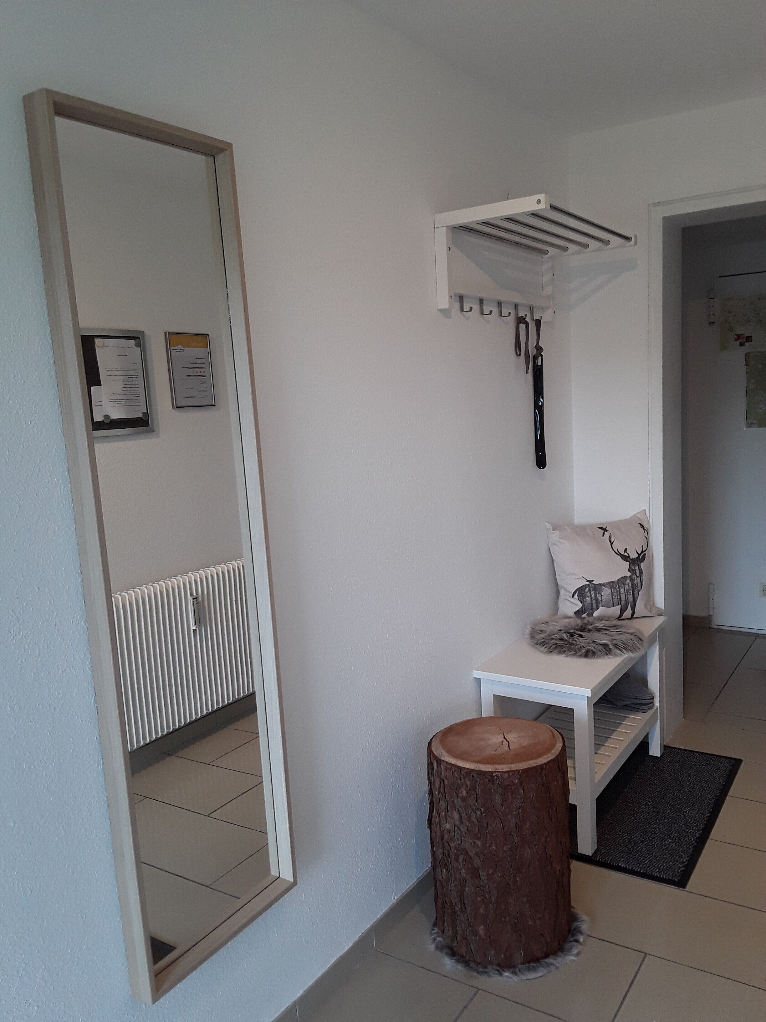 Quarto com um espelho grande, um banco branco com almofada de veado, um radiador e um banquinho de madeira.