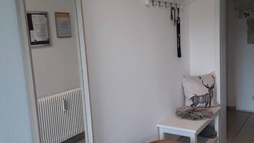 Quarto com um espelho grande, um banco branco com almofada de veado, um radiador e um banquinho de madeira.