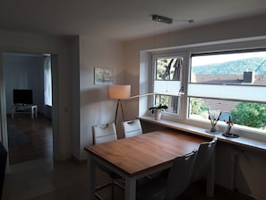 A dining area with a wooden table and chairs, a lamp, and a window with a view of buildings and trees.