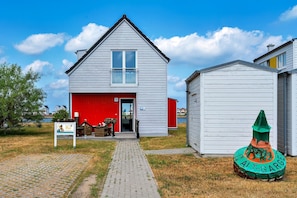 Een gebouw met twee verdiepingen, een rode garageklep, een kleine schuur en een groen bord met tekst.
