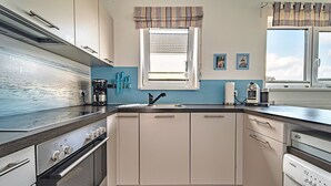 Una cocina equipada con estufa, horno, lavavajillas y una ventana con cortinas.