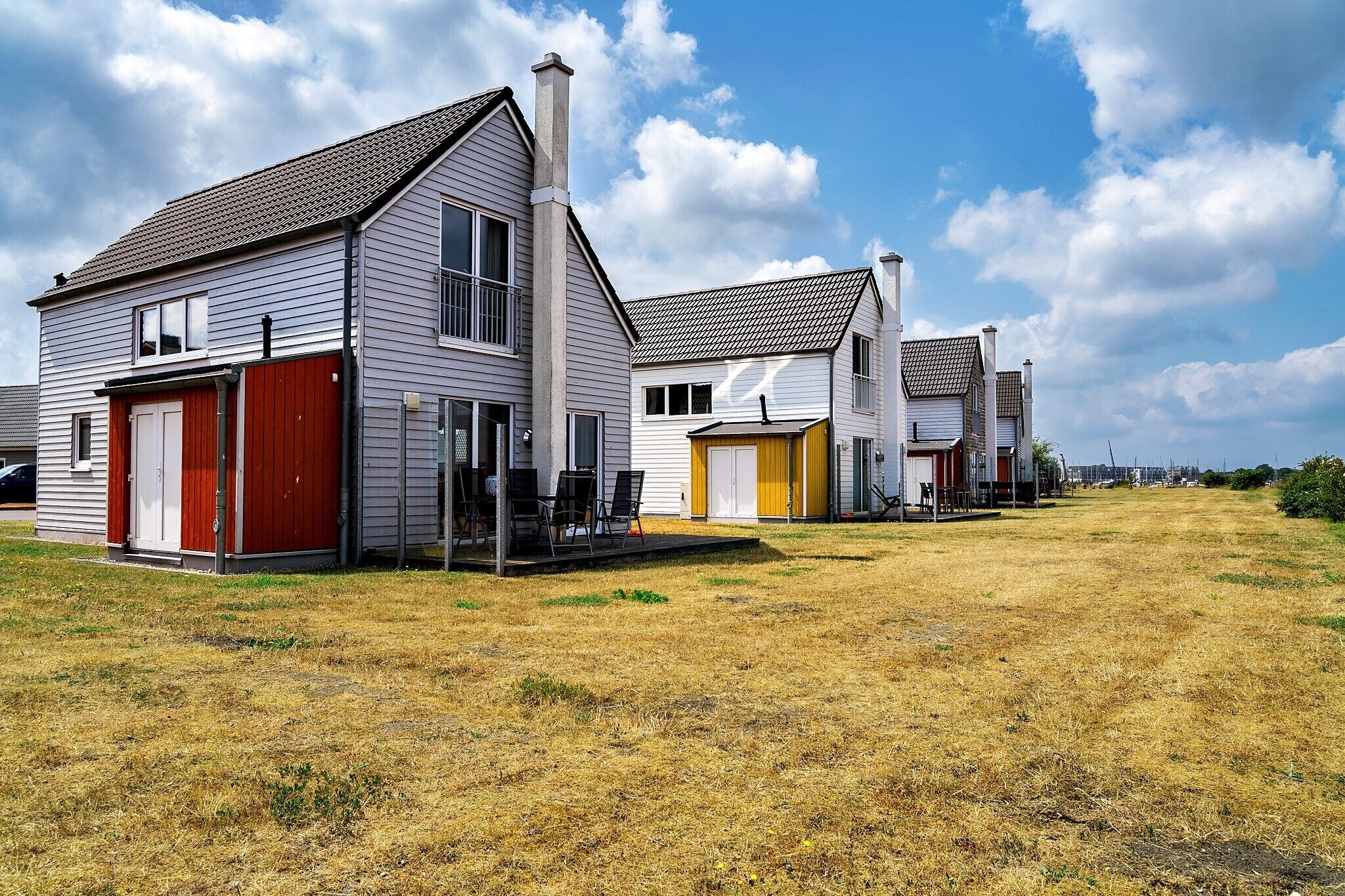 A row of single-story houses with attached garages, a grassy yard, and a clear sky.