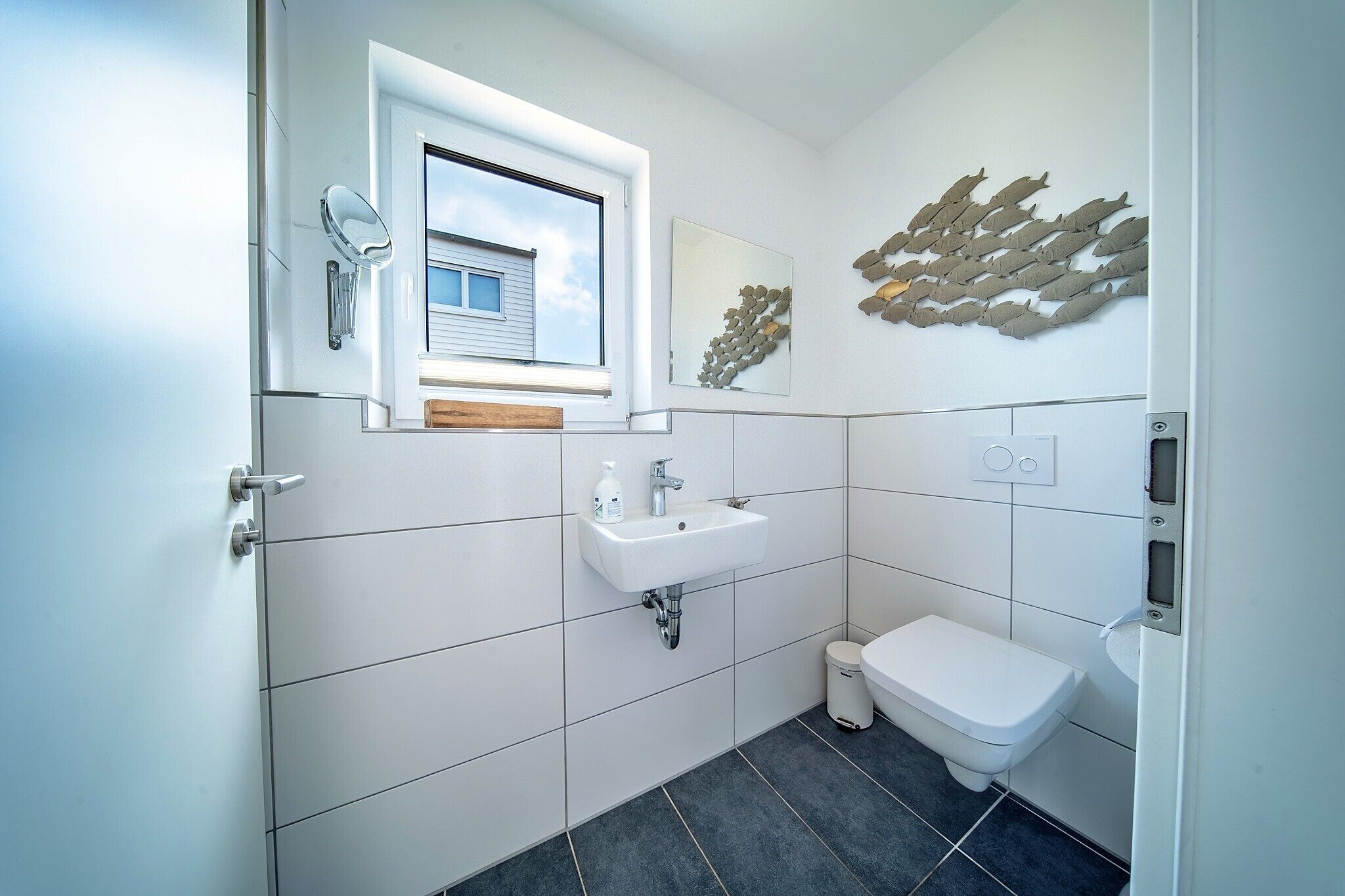 Een moderne badkamer met een raam, een wastafel, een toilet en een decoratief wandobject.