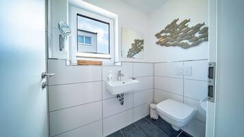 Een moderne badkamer met een raam, een wastafel, een toilet en een decoratief wandobject.