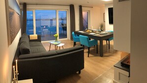 Una sala de estar moderna con sofá, mesa de comedor y sillas, un balcón con vistas y una chimenea.