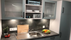 Una cocina con gabinetes grises, un lavamanos de acero inoxidable, una tabla de cortar de madera y un frutero.