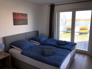 Un dormitorio con dos camas, un cuadro en la pared, una lámpara y vistas al exterior a través de una puerta corrediza.
