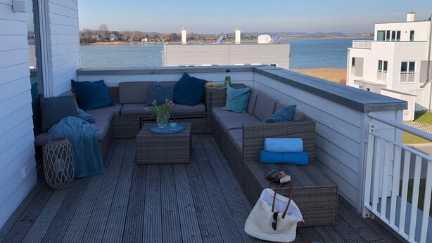 Una terraza con un sofá, cojines, una mesa con bebidas y un bolso.