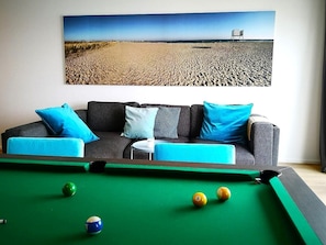 A pool table with balls, a sofa with cushions, and a painting of a beach scene.