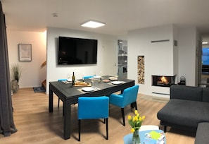A modern living room with a dining area, a flat-screen TV, a fireplace, and a sofa.