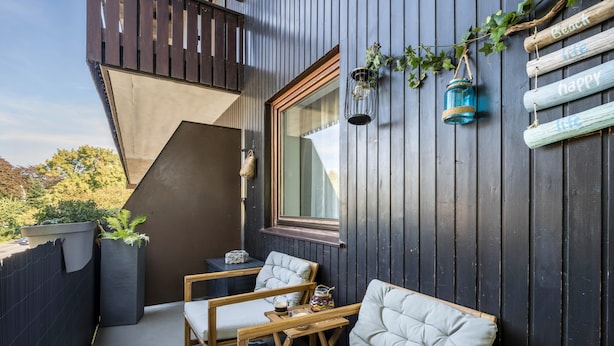A wooden deck with two cushioned chairs, a small table, and a window with a view of trees. - Holiday Apartment 'Time 2 Sea' with Shared Garden, Balcony and Wi-Fi (Scharbeutz)