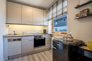Eine moderne Küche mit hellen Holzschränken, einem Einbauofen, einem Geschirrspüler und einem schwarzen Kühlschrank.
