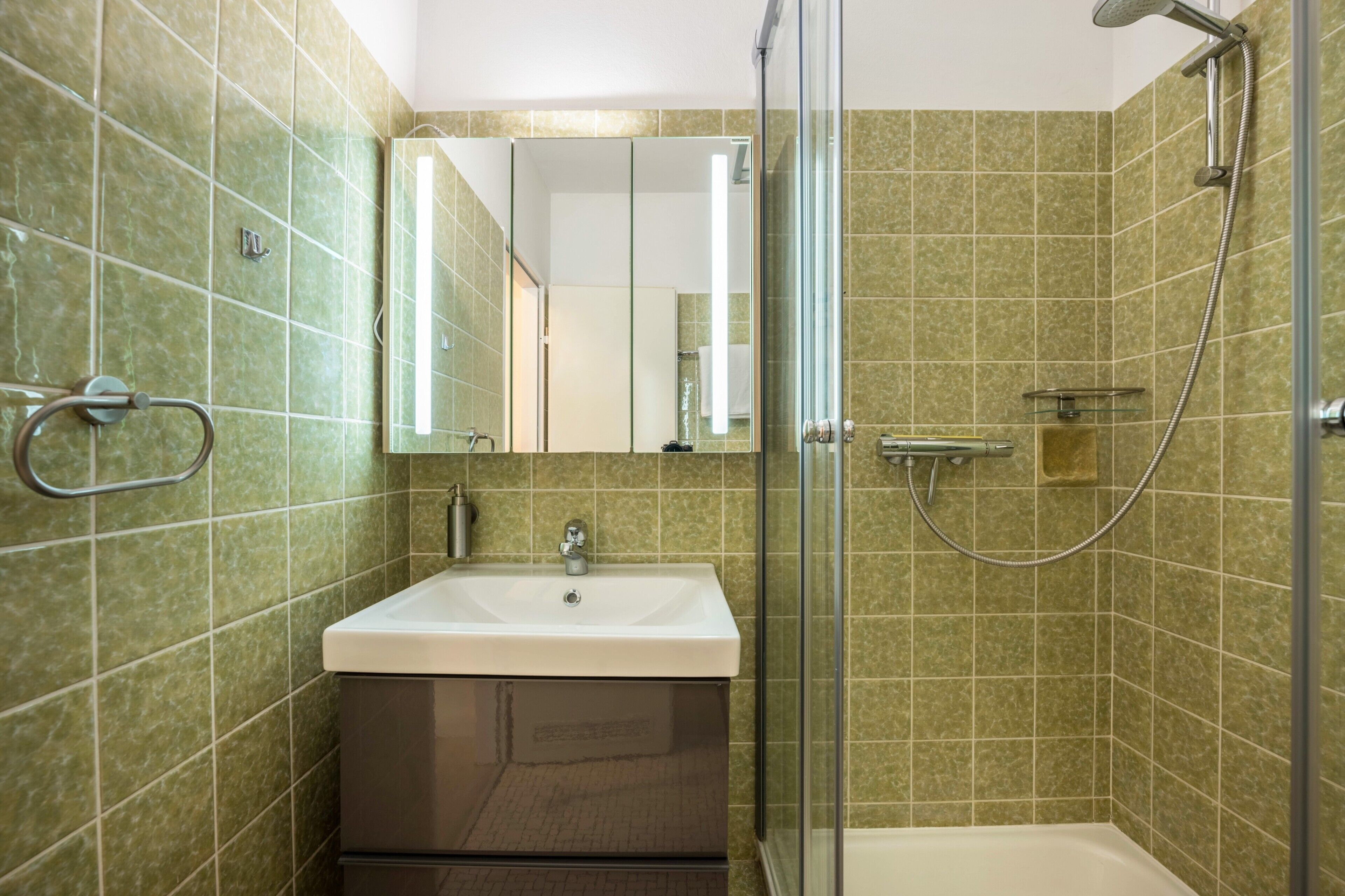 A bathroom with a glass shower enclosure, a sink, and a mirror.