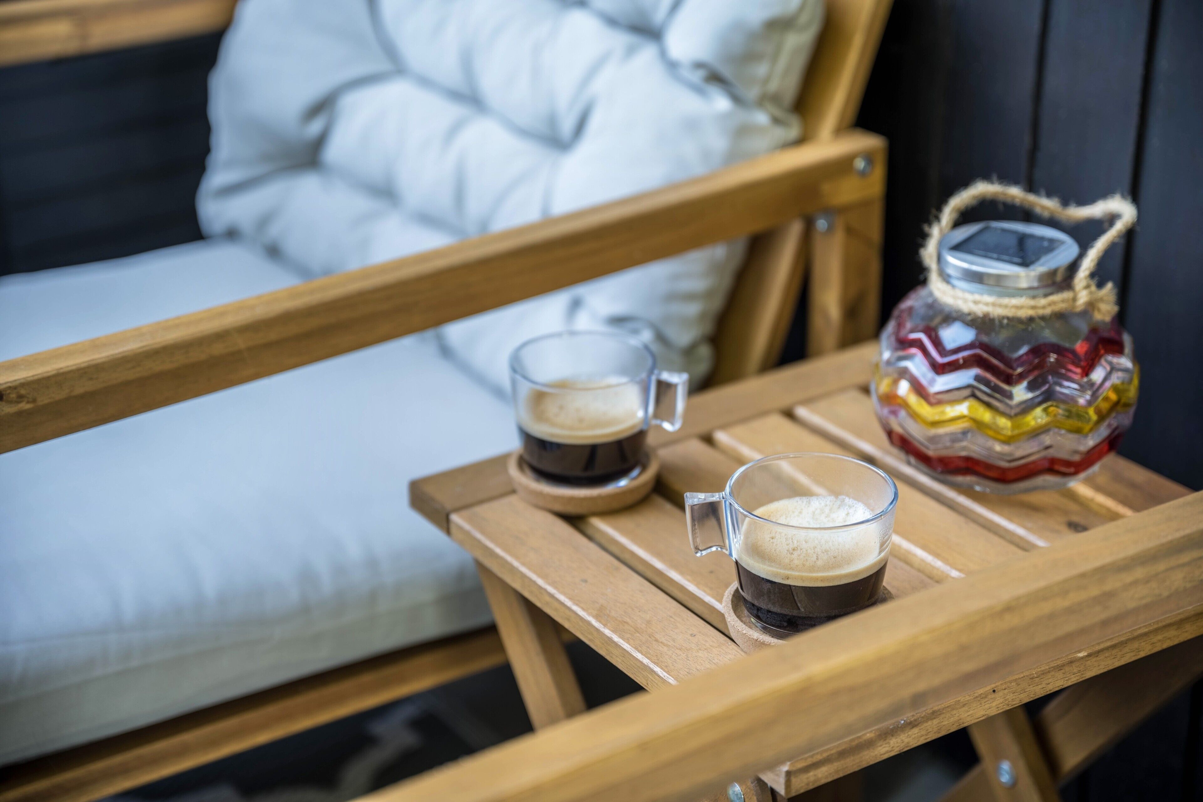 A wooden table with two glasses of coffee and a decorative jar.