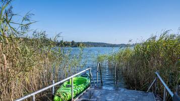 Ein Kajak liegt an einem Steg, mit freiem Blick auf einen See und entfernte Bäume.