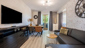 A modern living room with a flat-screen TV, a sofa, a coffee table, and a dining area with chairs and a table. - Holiday Apartment 'Time 2 Sea' with Shared Garden, Balcony and Wi-Fi (Scharbeutz)