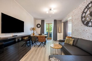 Uma sala de estar moderna com uma televisão de tela plana, um sofá, uma mesa de centro e um espaço de jantar com cadeiras e uma mesa.
