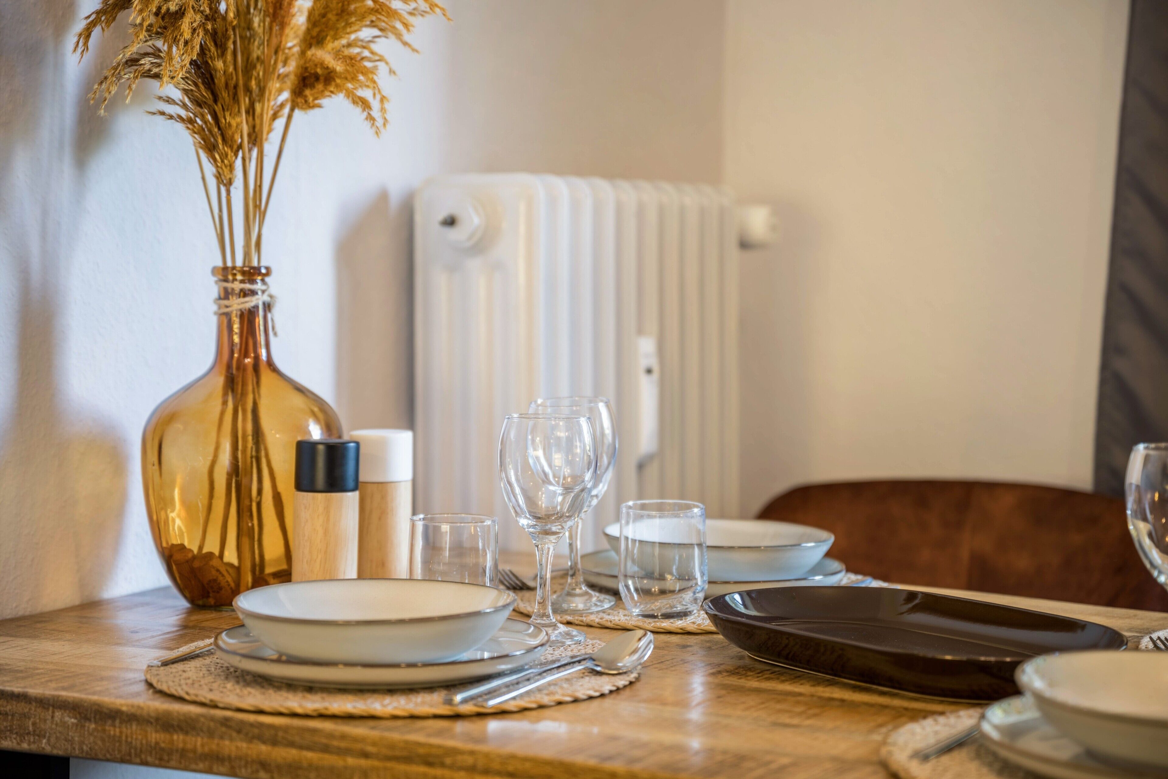 A dining table set with plates, glasses, and a vase with dried plants.