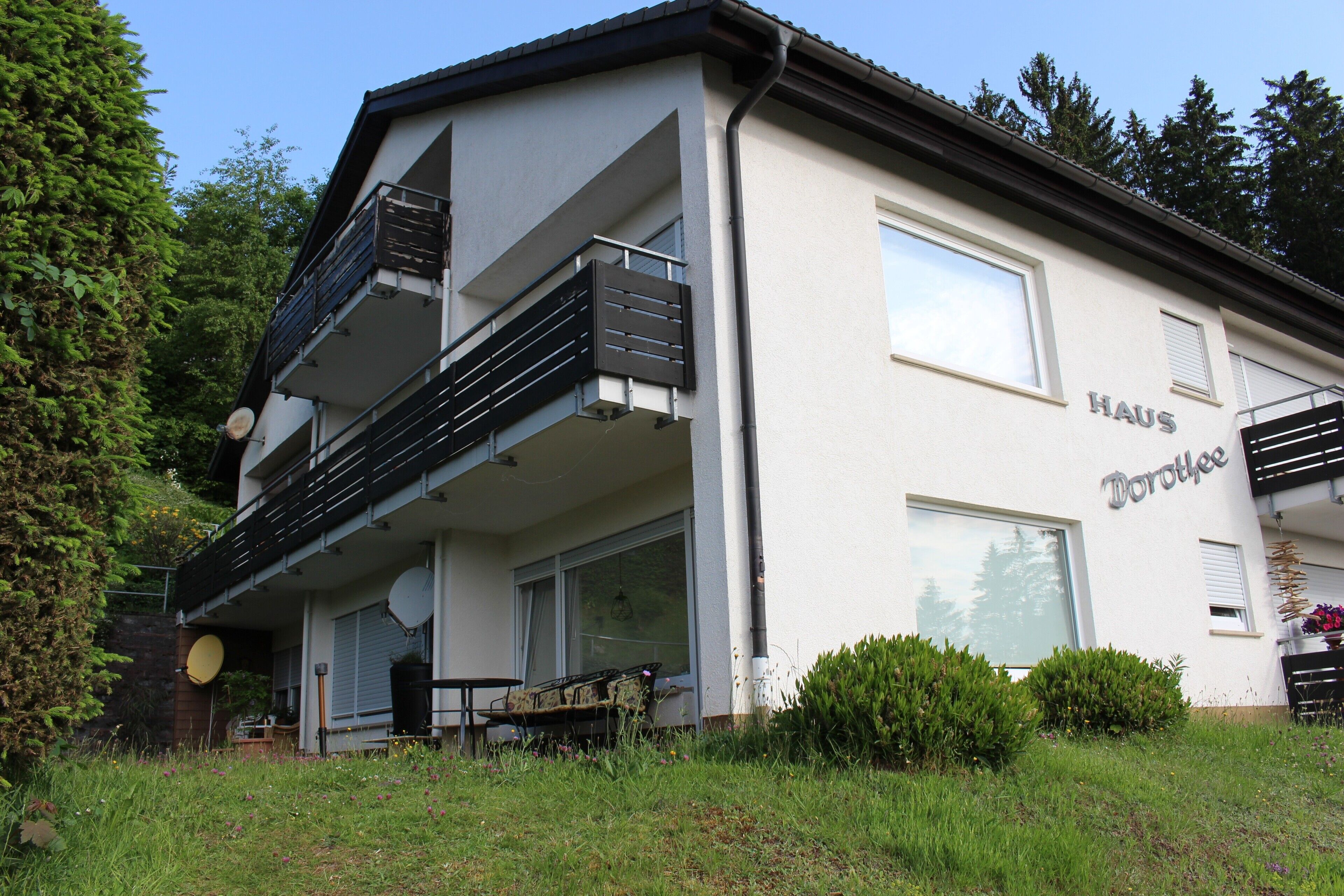 Ein zweistöckiges Gebäude mit einem Balkon und einer Satellitenschüssel. Auf der Seite ist der Schriftzug 'HAUS Dorothee' zu sehen.