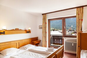 Ein Hotelzimmer mit Bett, Holz-Kopfteil, Nachttisch, Fenster mit Bergblick und Heizkörper.