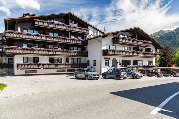 Ein mehrstöckiges Hotel mit Balkonen, einem Parkplatz und einer Bergkulisse.