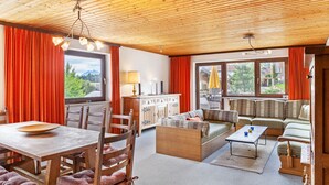 Techo de madera, una mesa de comedor con sillas, un sofá, una cama y una ventana con cortinas.