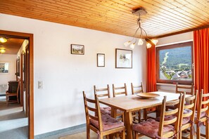 Zona pranzo con tavolo e sedie in legno, quadri appesi al muro e una finestra vista valle.