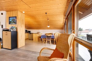 Un intérieur en bois comprenant un coin repas, une cuisine et un fauteuil en osier avec un coussin.
