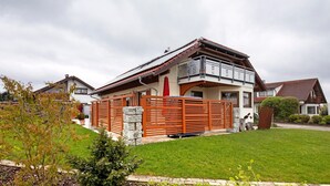 A two-story house with a red roof, a balcony, and a fenced yard. - Apartment 'Haus Bross' with Balcony and Wi-Fi (Hayingen)
