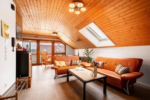 Uma sala de estar moderna com teto inclinado, vigas de madeira, um sofá, uma mesa de centro e um claraboia.