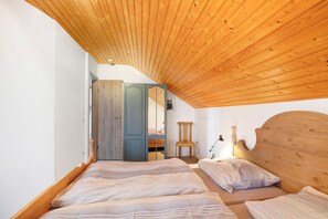 Une chambre avec un plafond en pente, une tête de lit en bois, deux lits, une chaise et une armoire.