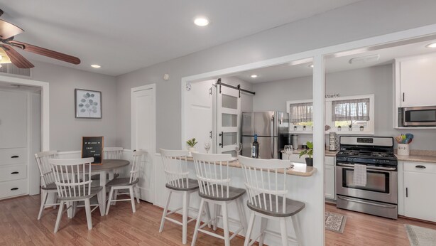 A modern kitchen with white cabinetry, a stainless steel refrigerator, and a built-in oven. There is a dining area with white chairs and a small table. - Charming Bungalow in the heart of Phoenix/Biltmore area.  (Phoenix)