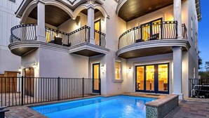 Un hotel con piscina, mobiliario exterior y un balcón de dos pisos con barandillas negras.