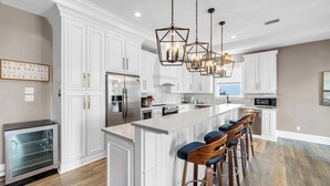 Una cocina moderna con armarios blancos, una isla central con taburetes altos y lámparas colgantes.