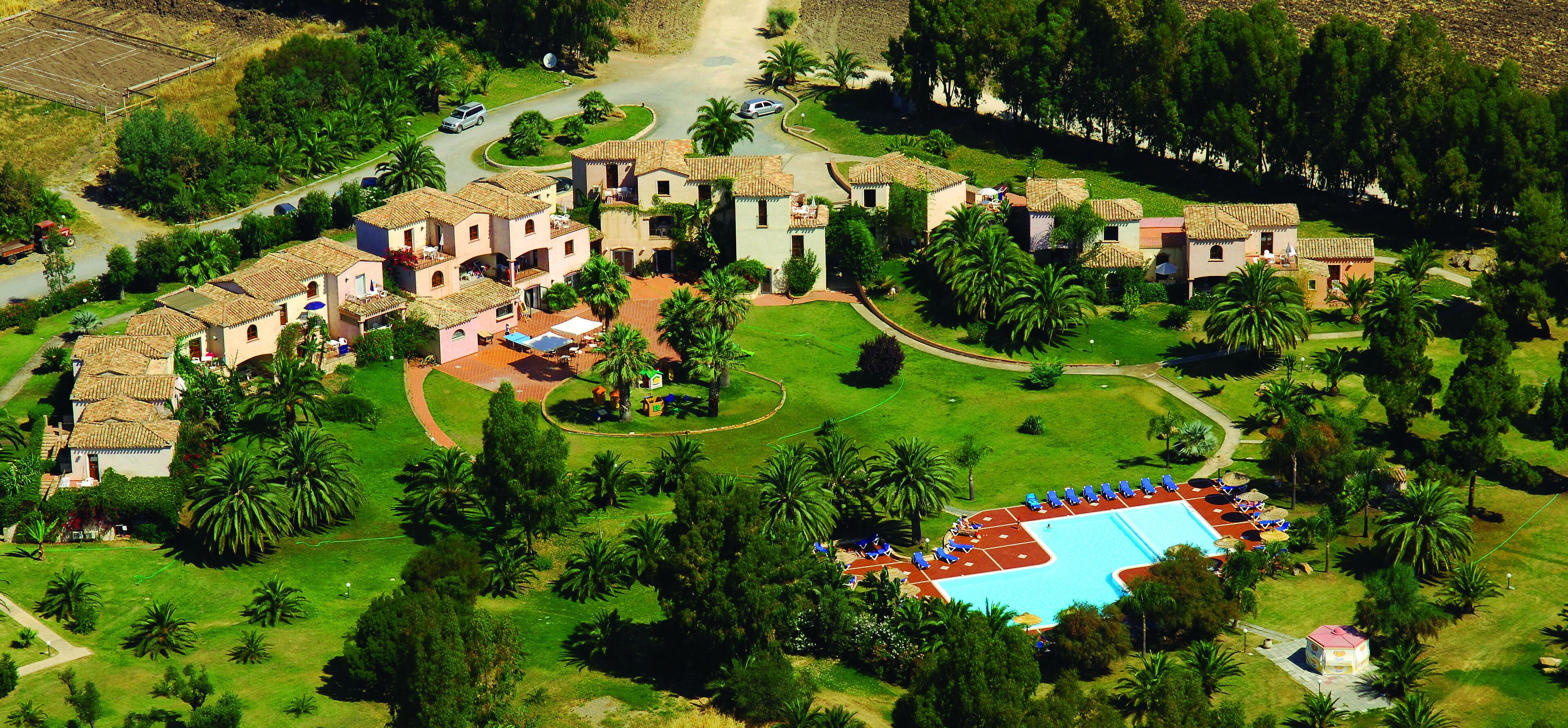 An aerial view of a resort with multiple villas, a swimming pool, and lush greenery.