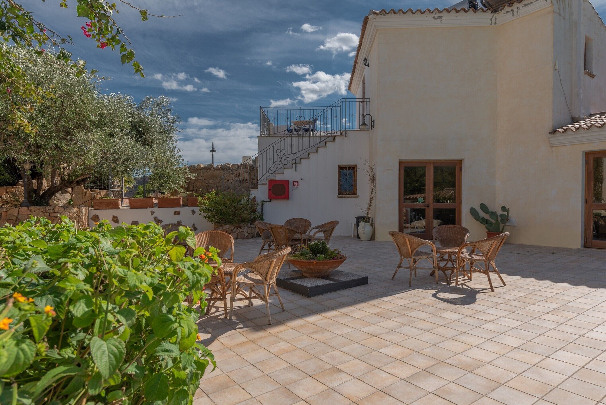 Un patio con mobiliario de mimbre, una planta en maceta y una escalera que sube a un nivel superior.