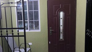A room with a dark wooden door, a window, a metal chair, and a welcome mat.