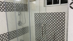 A glass-enclosed shower with a geometric tile pattern on the walls and a window with a grid design.