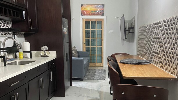 A compact kitchen with dark cabinets, a stainless steel sink, and a wooden dining table with chairs.