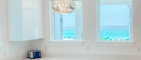 A modern kitchen with white cabinets, a stainless steel sink, and a view of the ocean through two windows.