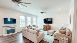 Ein geräumiges Wohnzimmer mit Kamin, zwei Sofas, einem Fernseher und Deckenventilatoren.