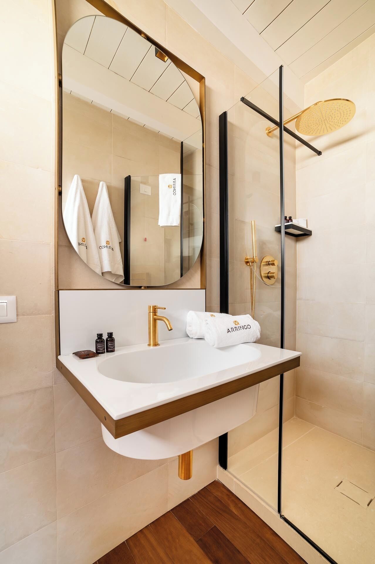 A modern bathroom with a large mirror, a gold faucet, and a glass-enclosed shower.