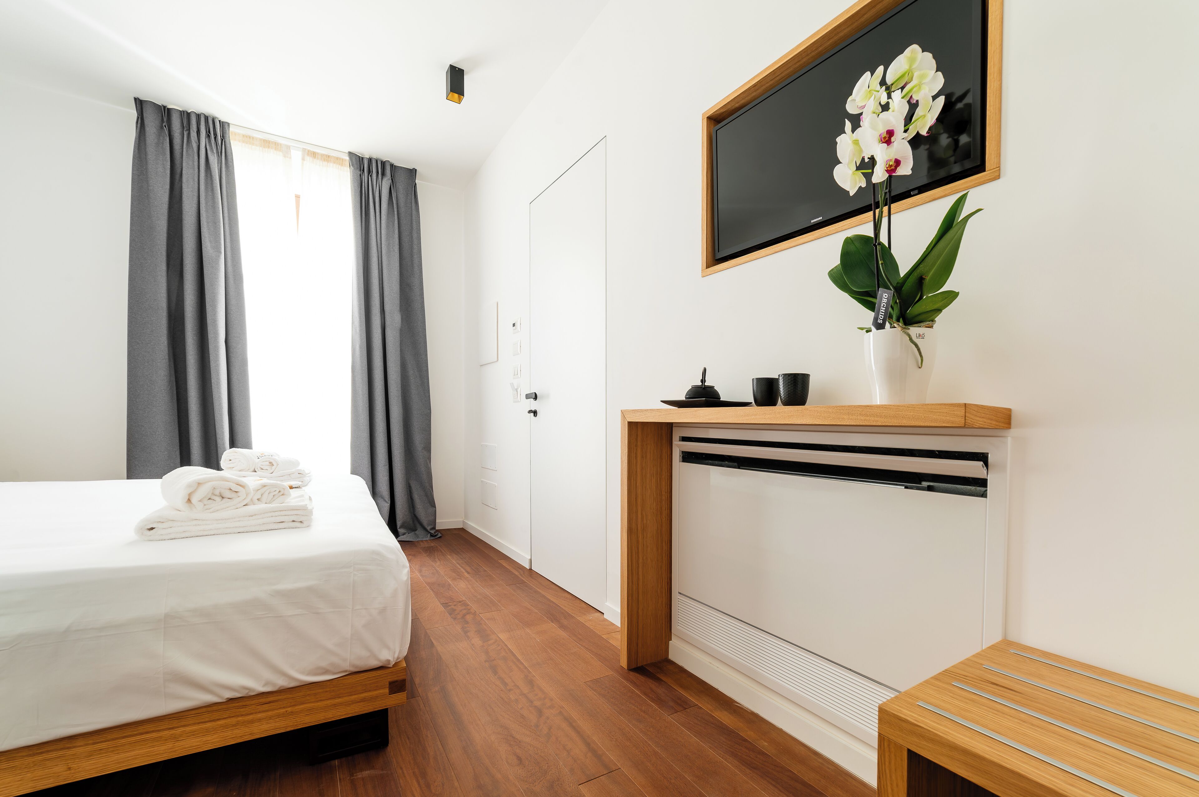 Habitación de hotel con cama, una mesita con un florero y un televisor montado, además de un radiador.