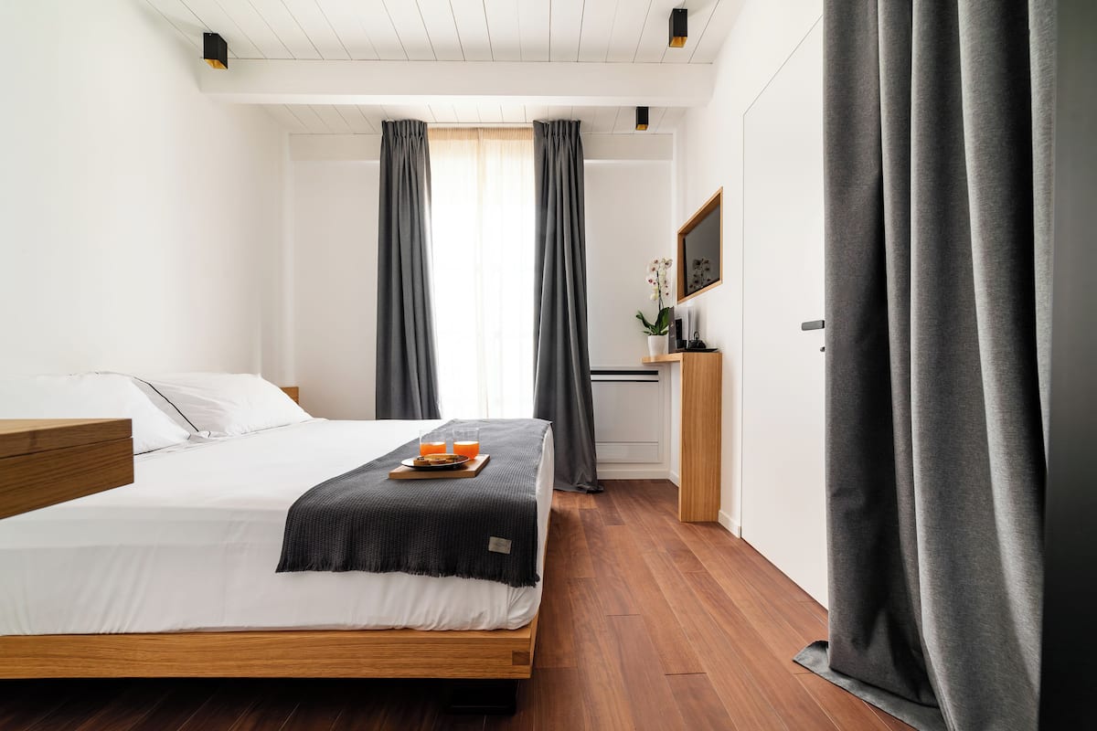 Et moderne hotelværelse med en træseng, et lille skrivebord med en plante, og et fjernsyn på væggen.
