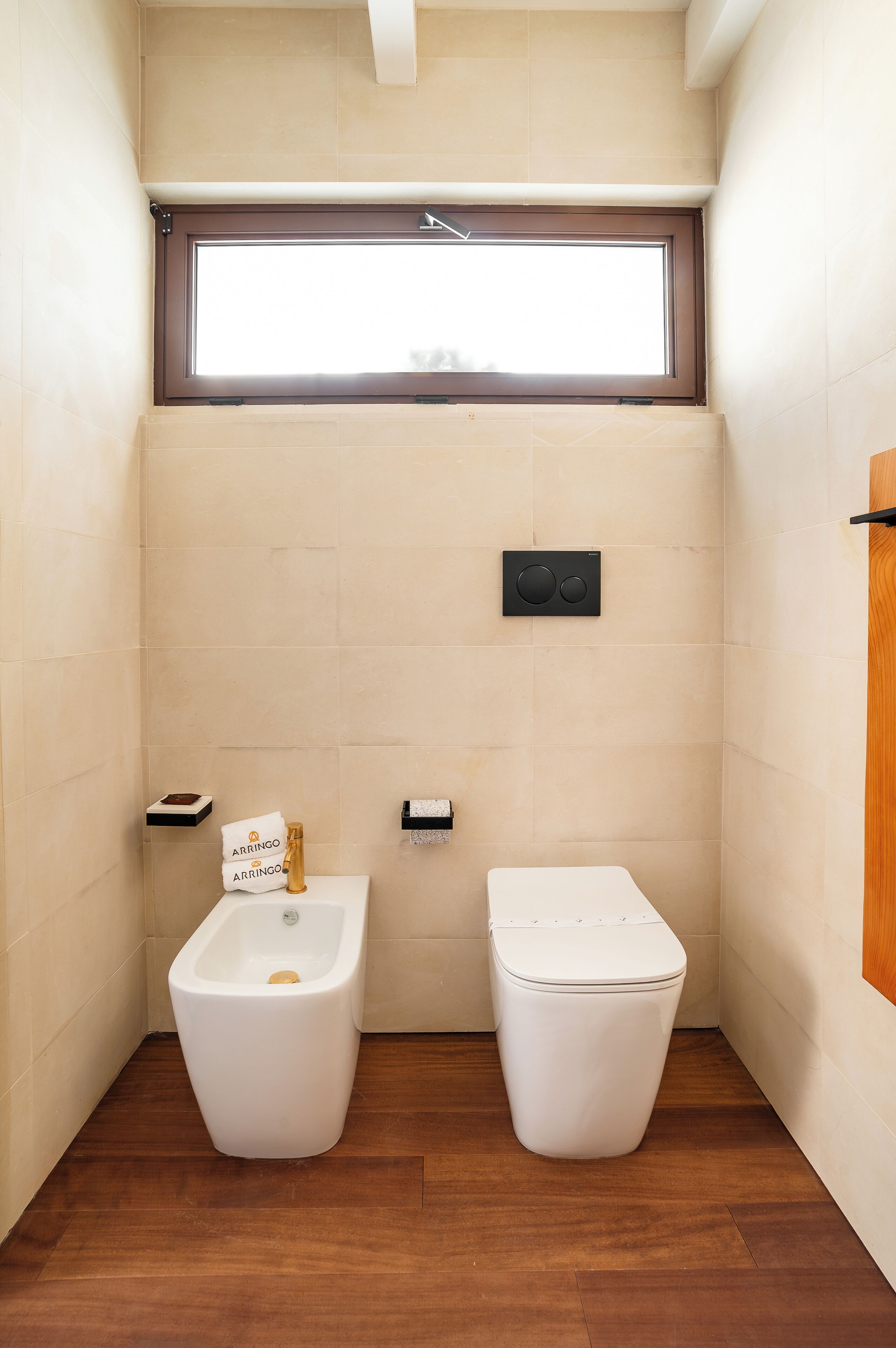 Et lille, moderne badeværelse med bidét, toilet og et vindue med naturligt lys.